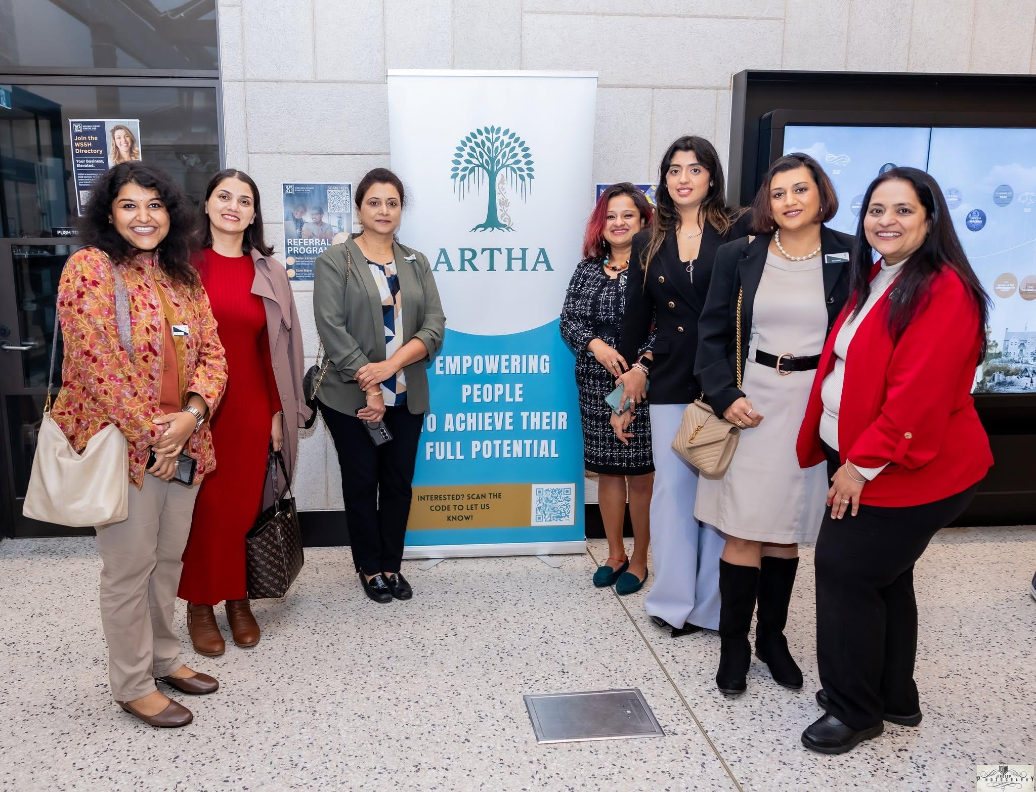 Seven members standing together beside the Artha banner at a community evening