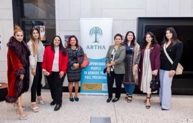 A group of women business owners beside the Artha banner at a community event.