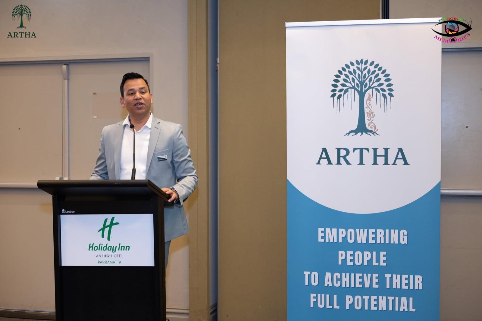 A speaker at the lectern beside the Artha banner at the Soft Launch Event.